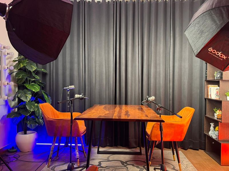 Professional podcast studio in Rajouri Garden, West Delhi with wooden table, two orange chairs, RØDE PodMics and Godox softbox lights